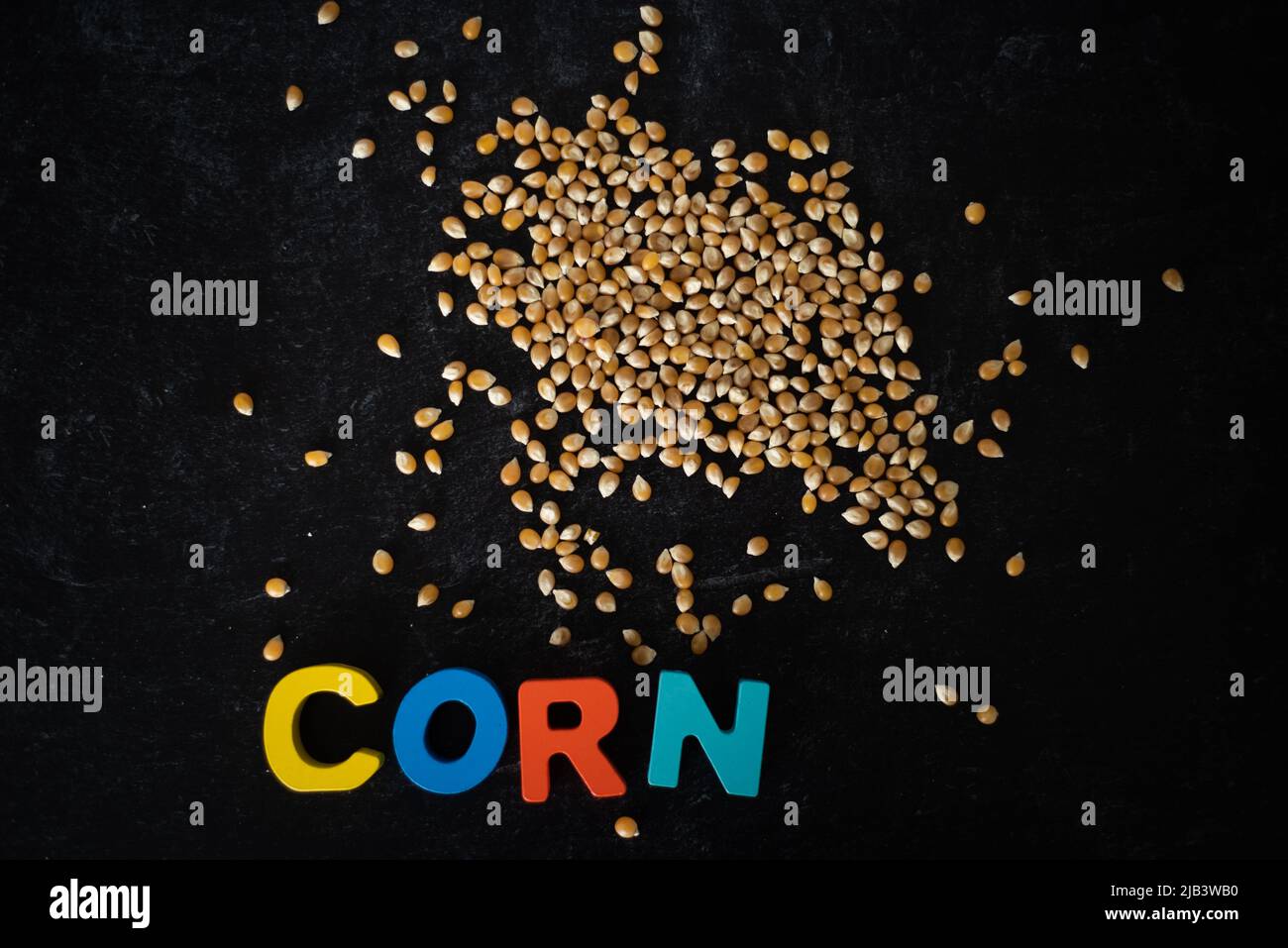 Top view of corn kernels with wooden colored letters spelling CORN on dark moody background