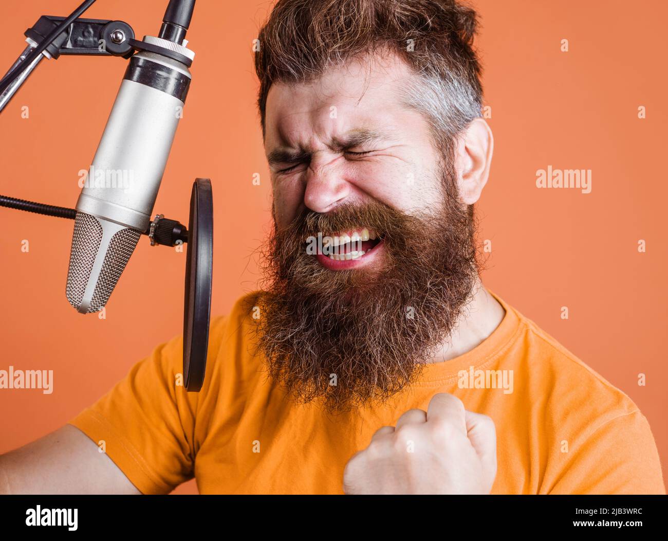 Bearded man sings in condenser microphone at recording studio. Emotional Male professional vocalist. Stock Photo