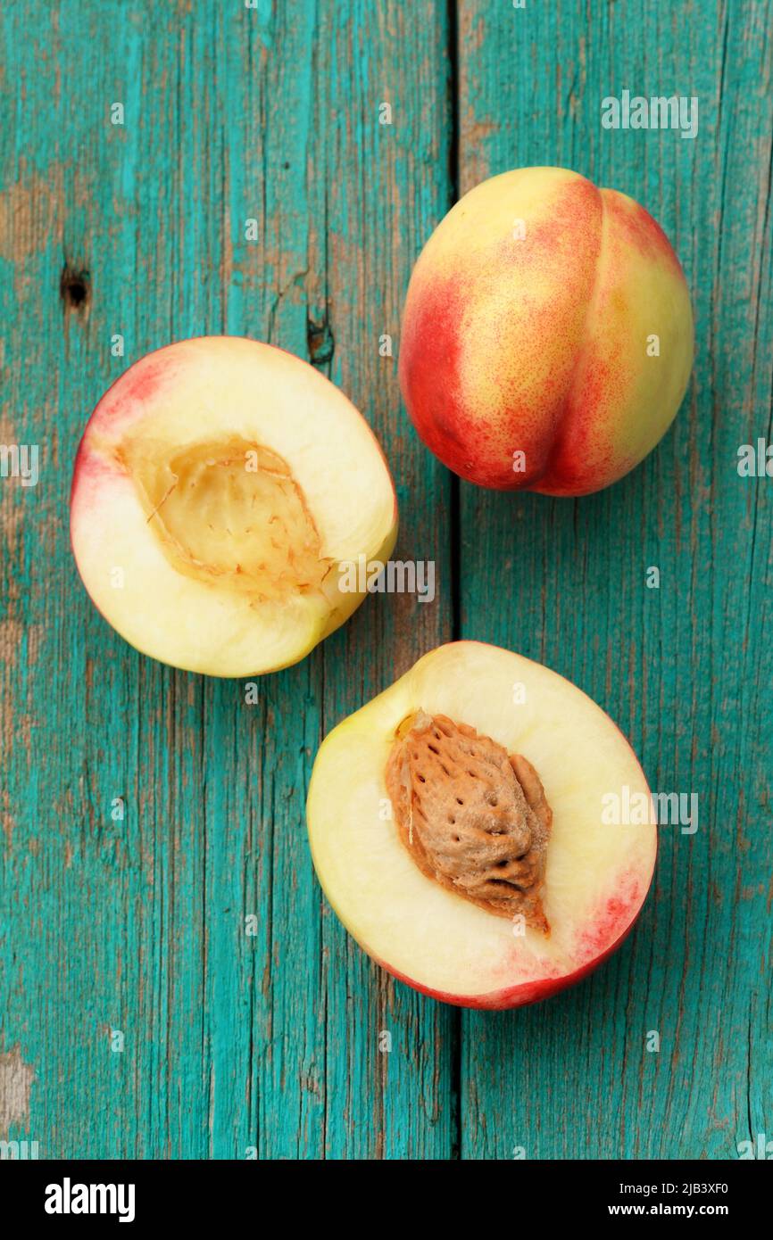 Two nectarines, whole and split on vintage turquoise table vertical Stock Photo