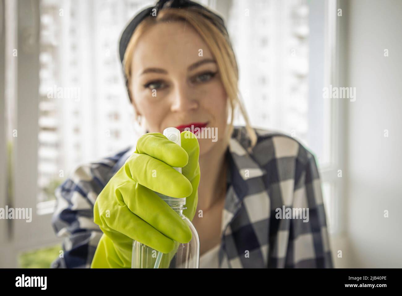 Pretty woman sprays window cleaner on glass. Stock Photo