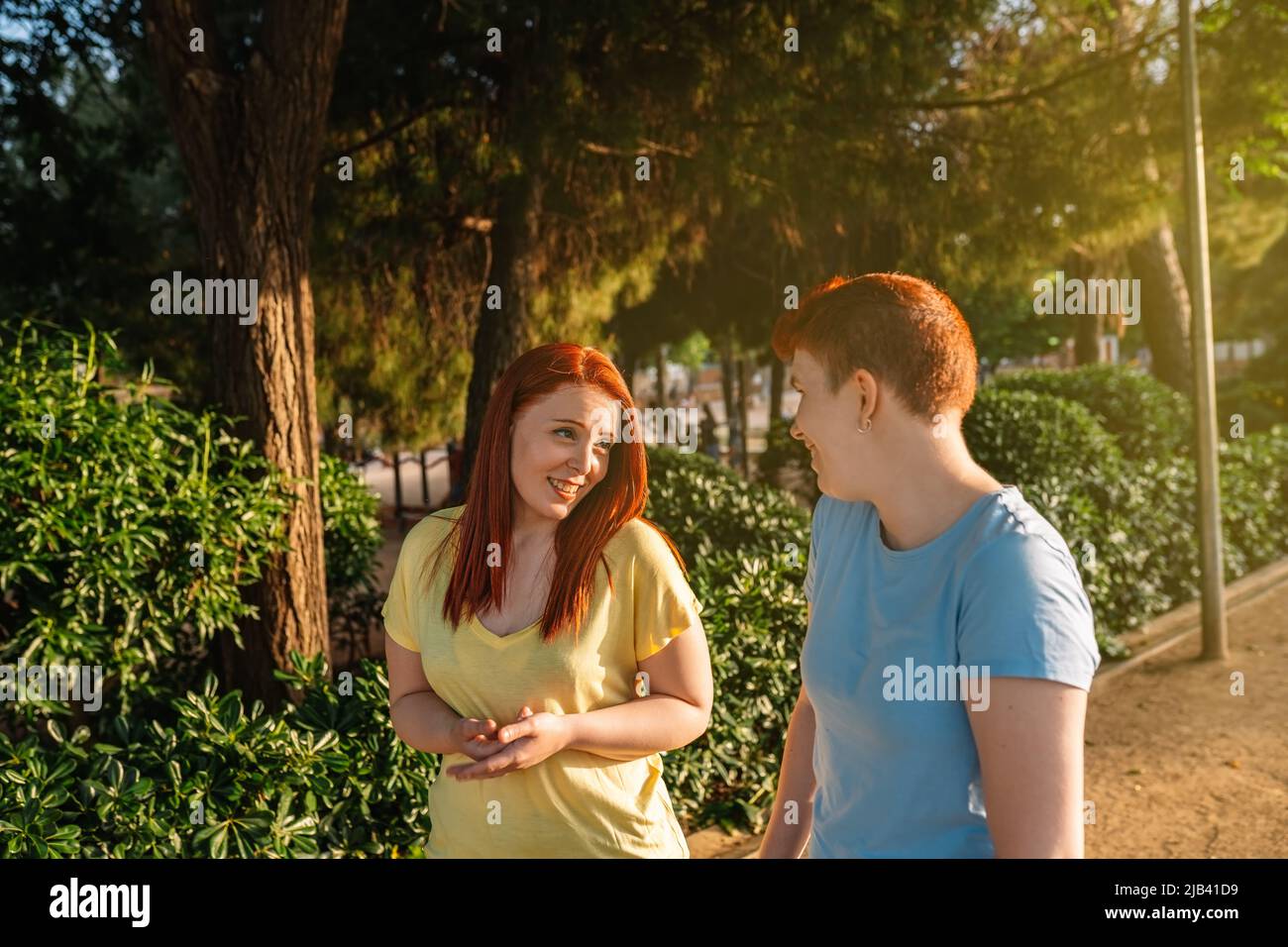 two young people chatting and strolling happily, in a public park in the city at dawn. young girls enjoying the summer outside. concept of friendship Stock Photo