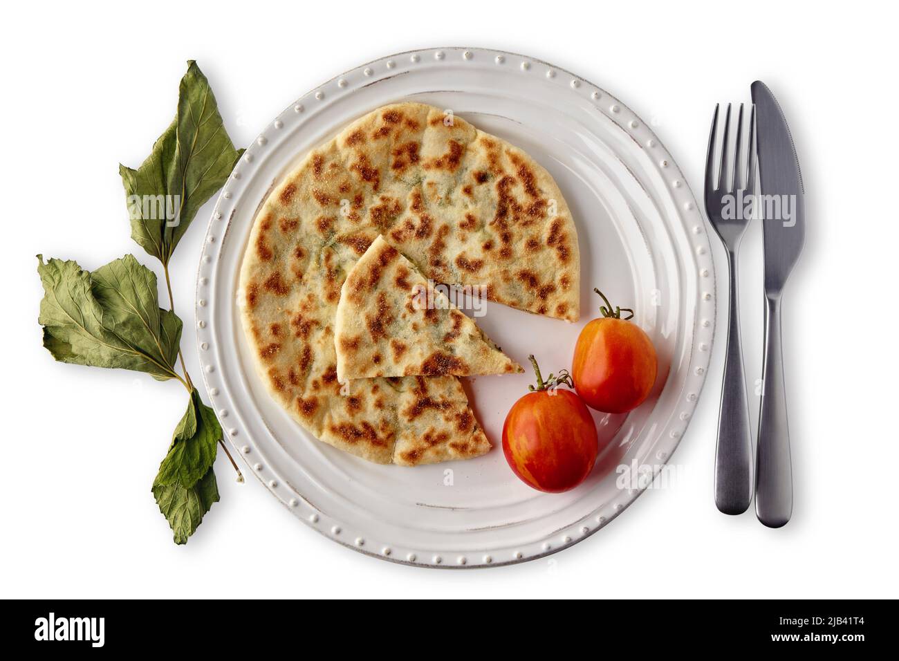 Flatbreads with cheese and herbs on a white plate with cutlery, decorated with tomatoes and dried currant leaves, isolated on a white background. Top Stock Photo