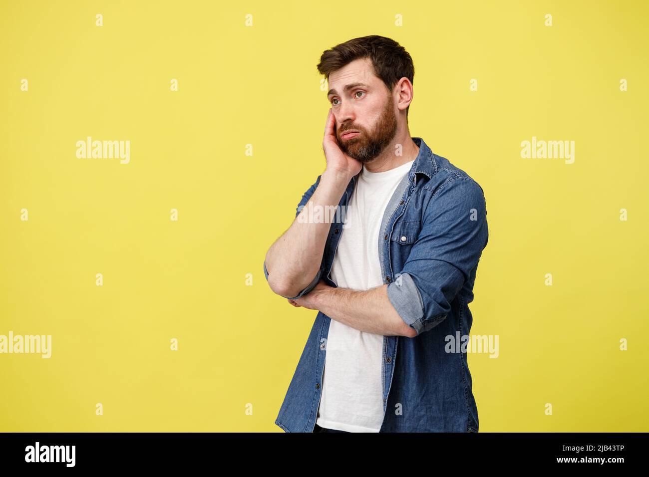 Upset man thoughtfully holding his beard on yellow background Stock Photo