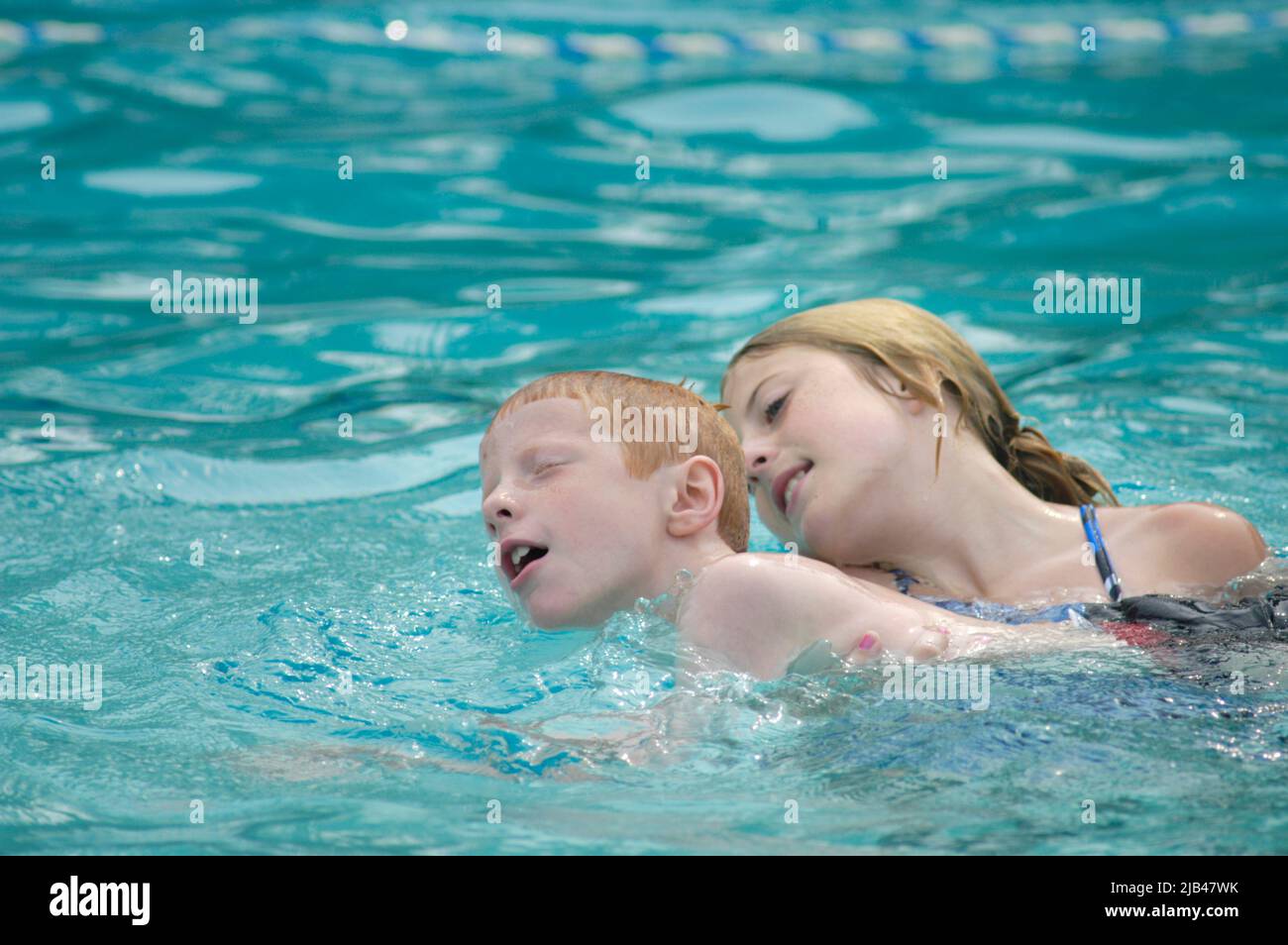 Brother and older sister in Pool playing in water as she teaches him ...