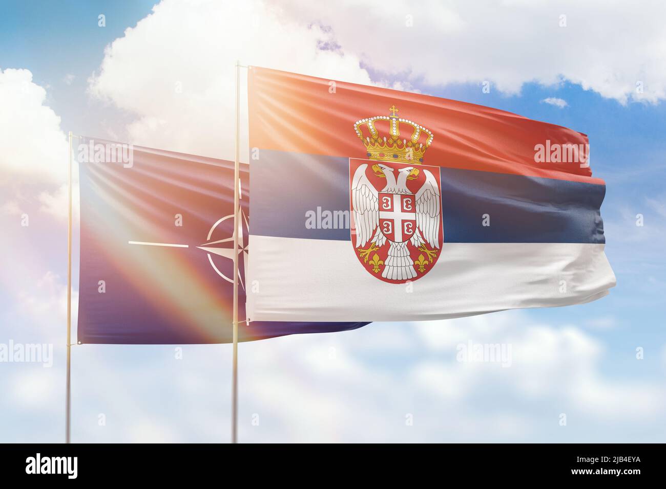 Sunny blue sky and flags of serbia and nato Stock Photo