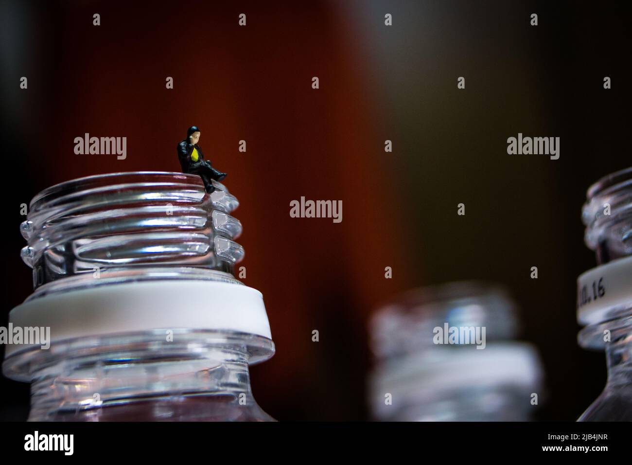 Miniature business man sitting on the plastic bottle's neck. The man in image is making a phone call with his mobile phone. Stock Photo