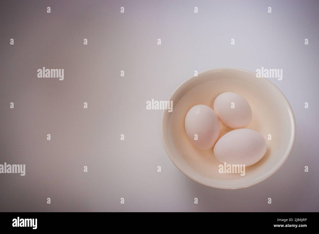 Three eggs on bowl on plain white background with copy space. Stock Photo
