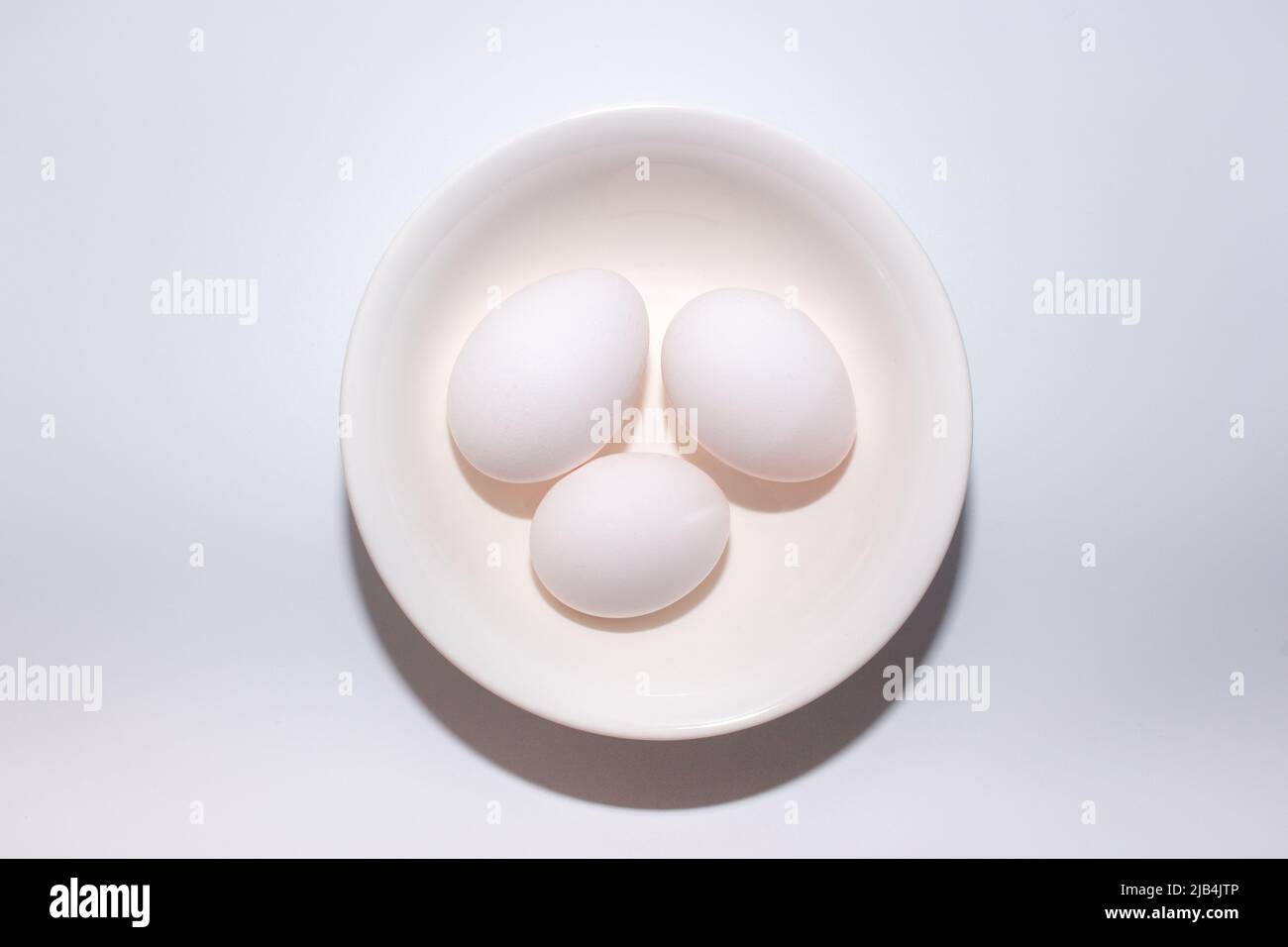 Three eggs on bowl from vertical view on plain white background. Stock Photo