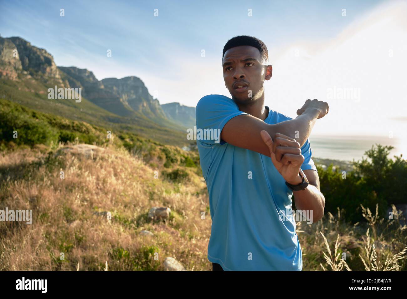 Black young African American Adult male focussed and stretching before his morning exercise on the beautiful mountain. Working out outdoors Stock Photo