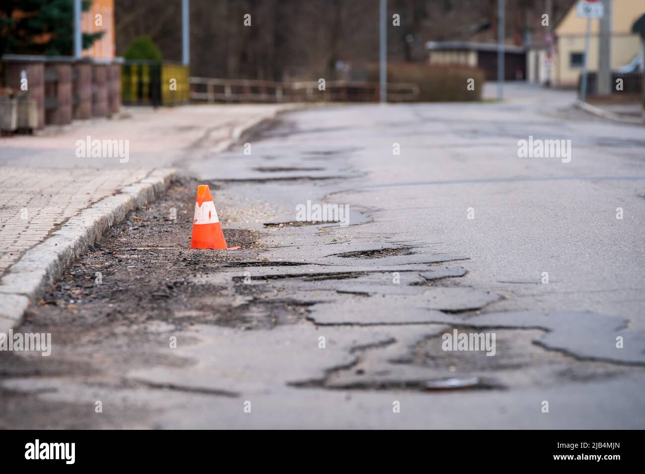 Damaged asphalt pavement road with potholes and traffic cone Stock Photo