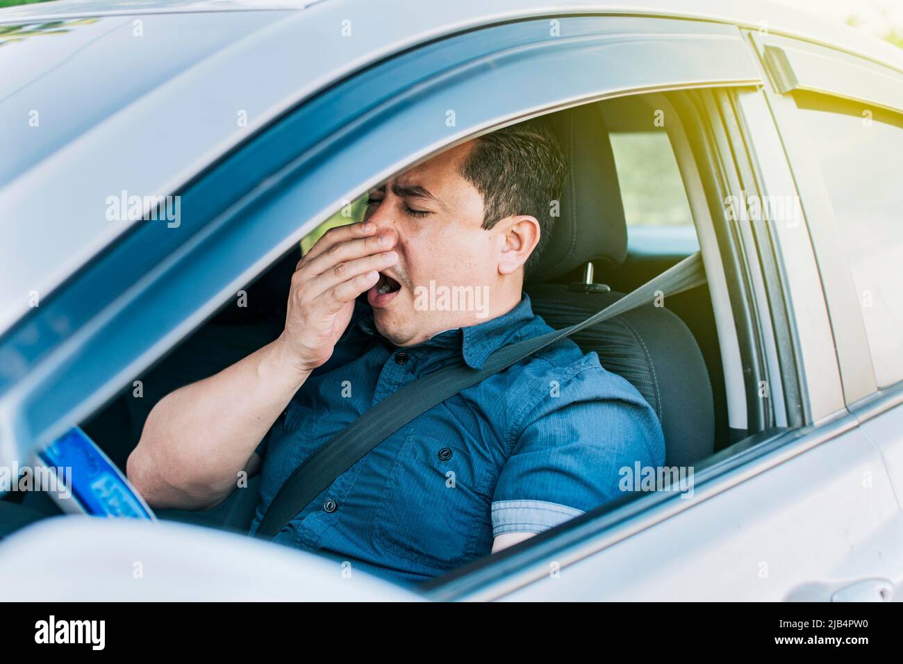 A sleepy driver at the wheel, a tired person while driving, Tired driver yawning, concept of man yawning while driving Stock Photo