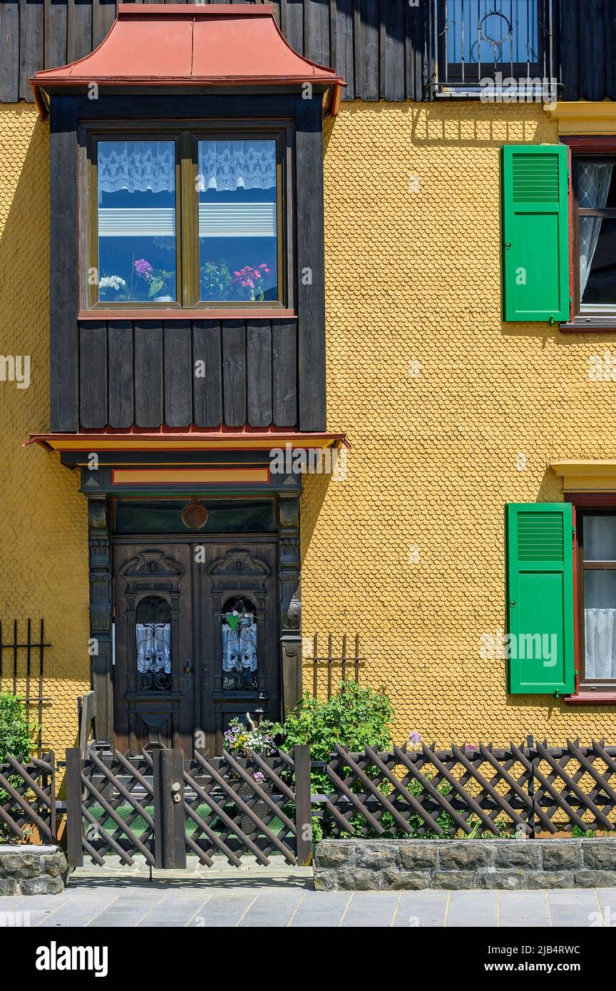 Yellow wooden shingle facade with bay window and green shutters, Oberstaufen, Allgaeu, Bavaria, Germany Stock Photo