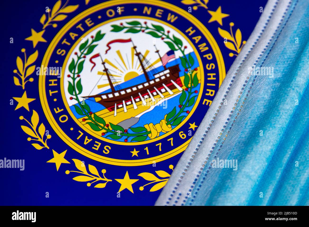Facial Mask on Flag and seal of New Hampshire. Several communities in NH require that face coverings be worn in public, effective November 20 in 2020. Stock Photo