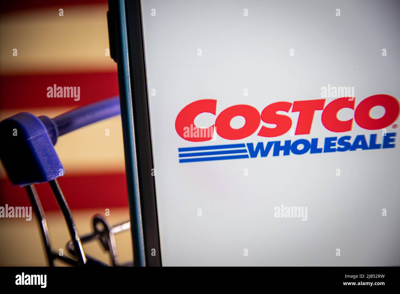 Logo of Costco, an US multinational corporation operates a chain of membership-only warehouse clubs, on iPhone in shopping cart with US flag. Stock Photo