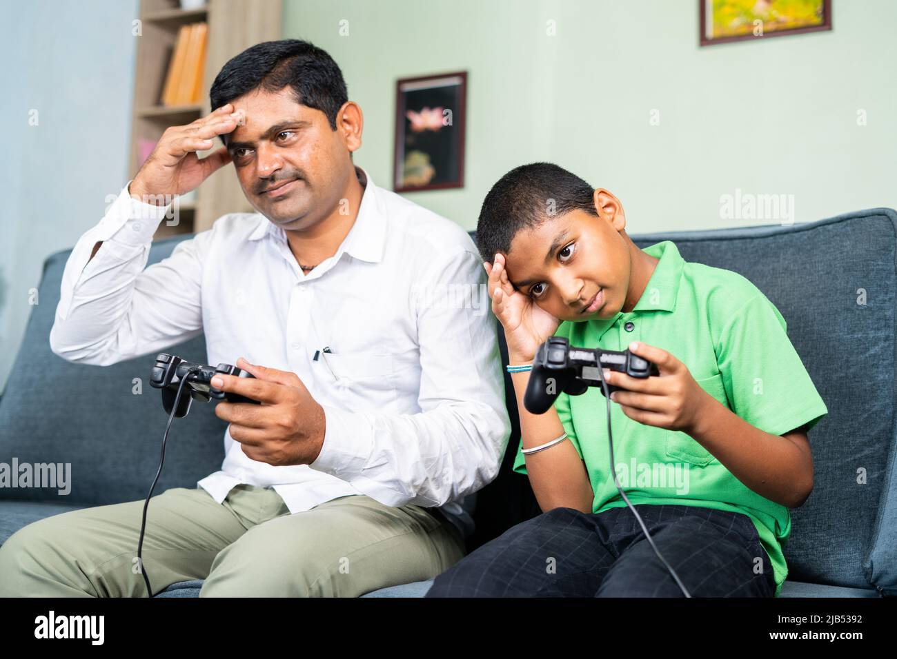 Young father and teenager kid lost game while playing video game using game pad at home on sofa - concept of entertainment, weekend holiday and family Stock Photo