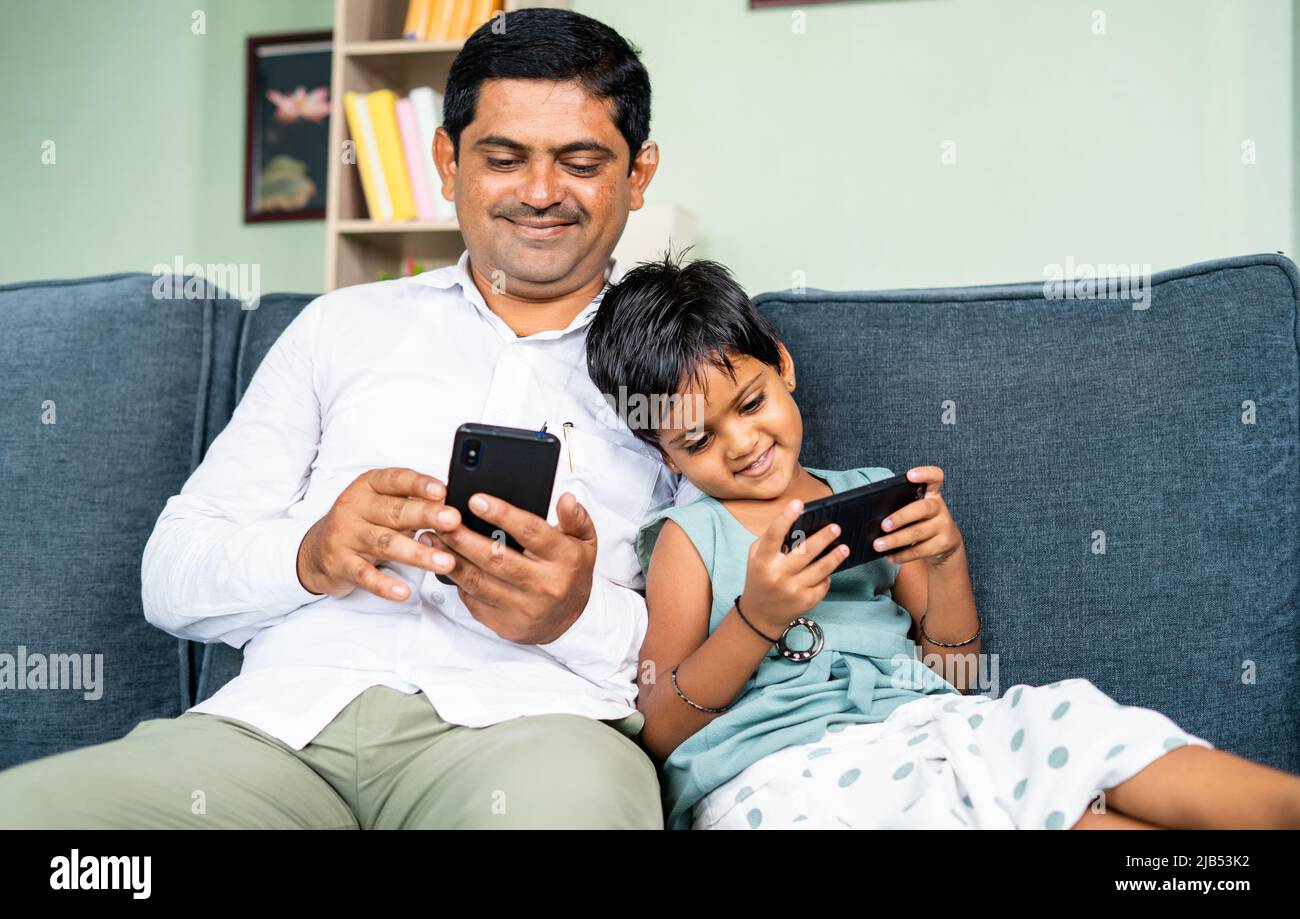 focus on kid Young father and kid by leaning busy using mobile phone while sitting on sofa - concept of technology, social media and internet Stock Photo