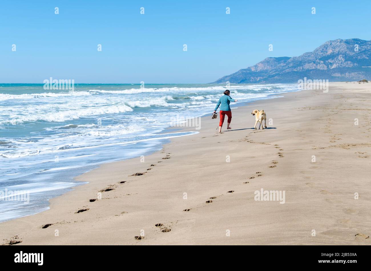 Footprints on the sand foot of a girl walking with sneakers in hand. Girl running with a dog on the Patara beach, Turkey Stock Photo