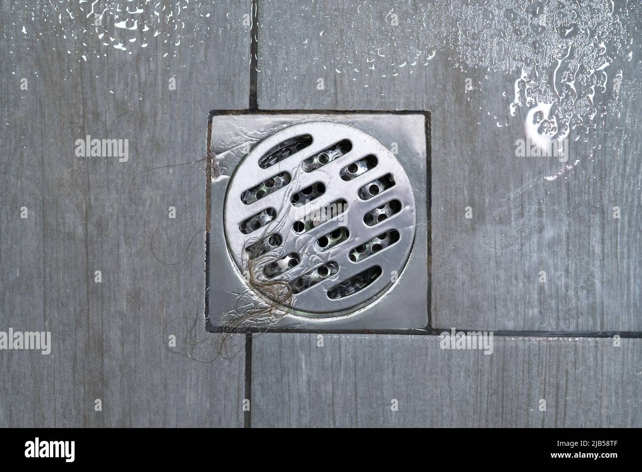 Metal shower drain cup to blockage on floor of bathroom with female hair clump after taking