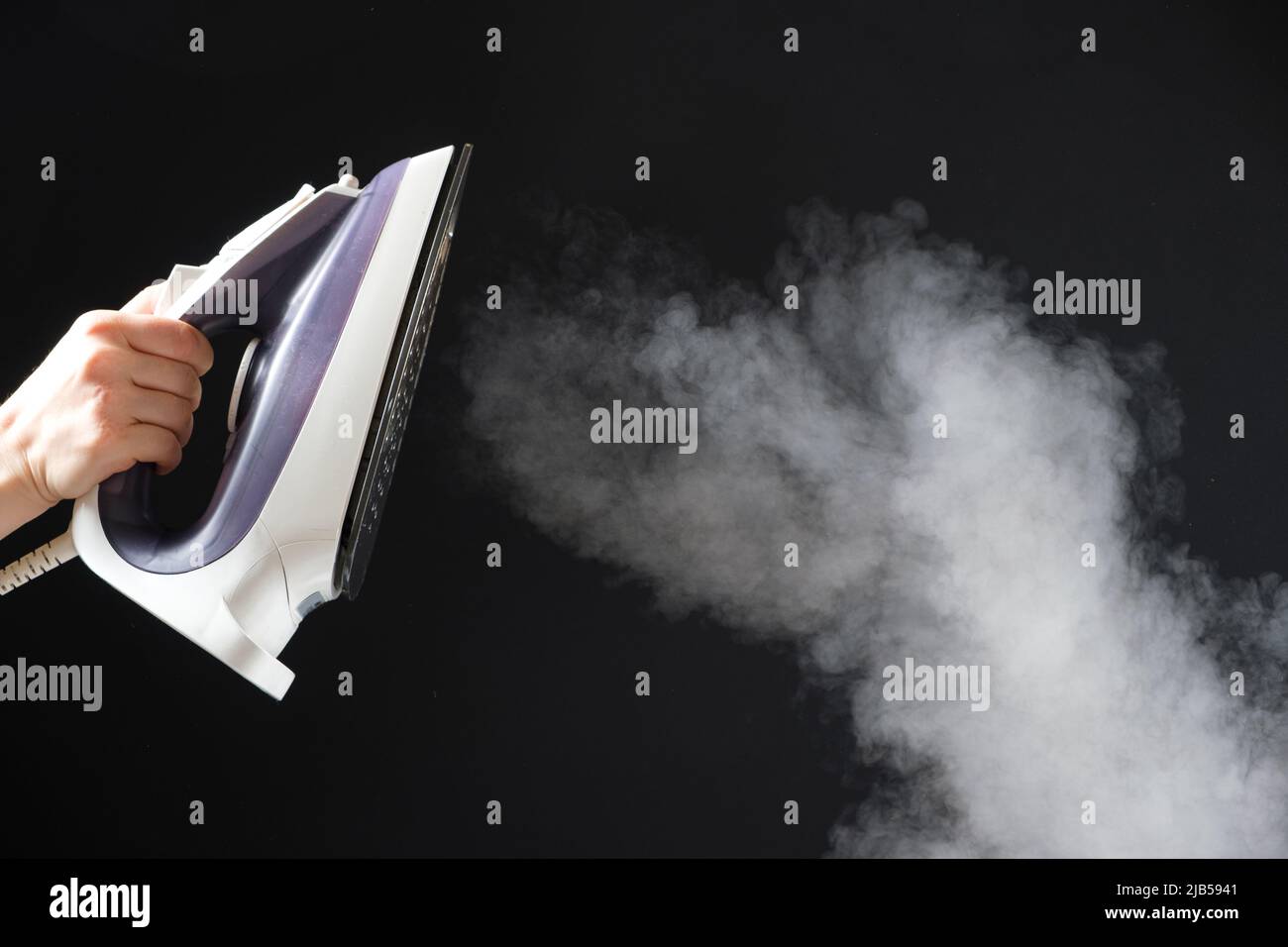 An iron with a steam generator sprays white hot steam on a black