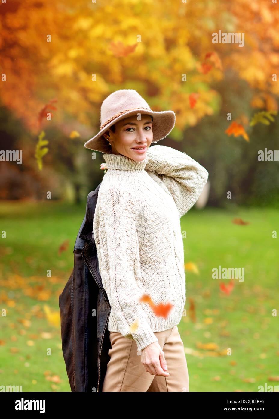extravagant woman in white sweater and hat walking in autumn park Stock Photo