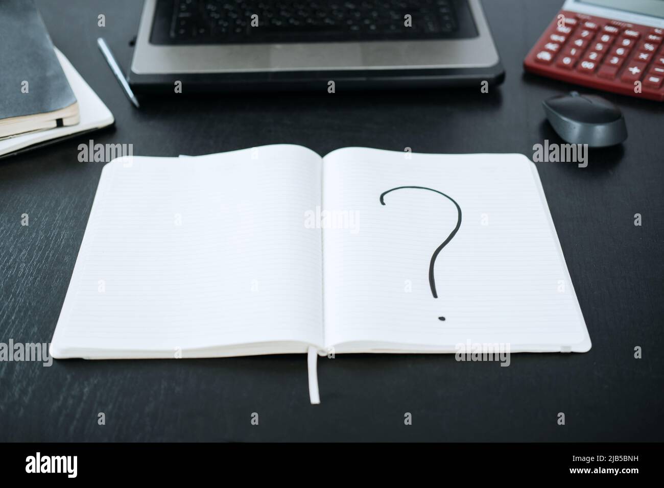 Question mark in a notepad on the background of a laptop and a