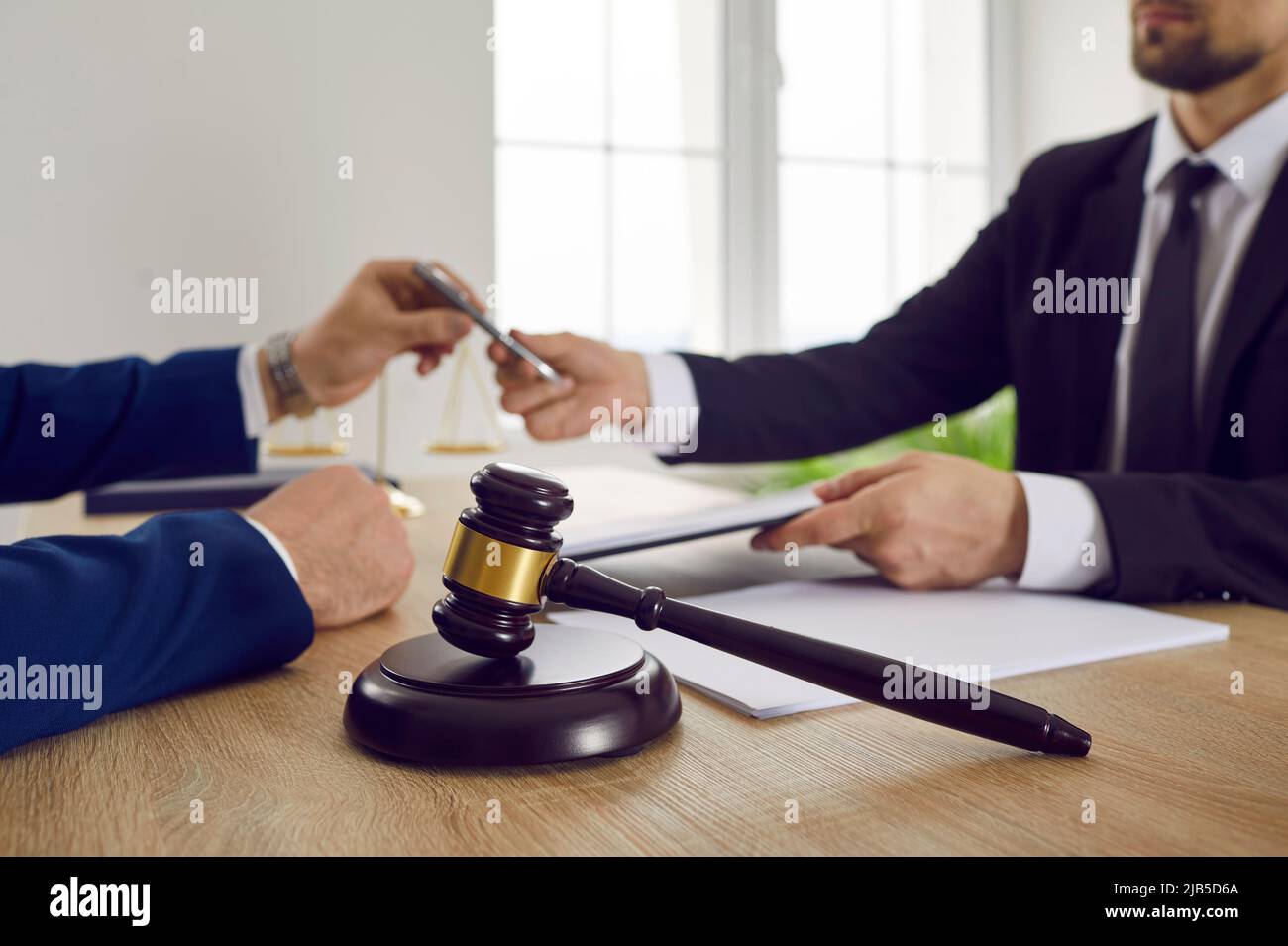 Wooden brown gavel of judge against background of lawyer and client signing legal contract. Stock Photo