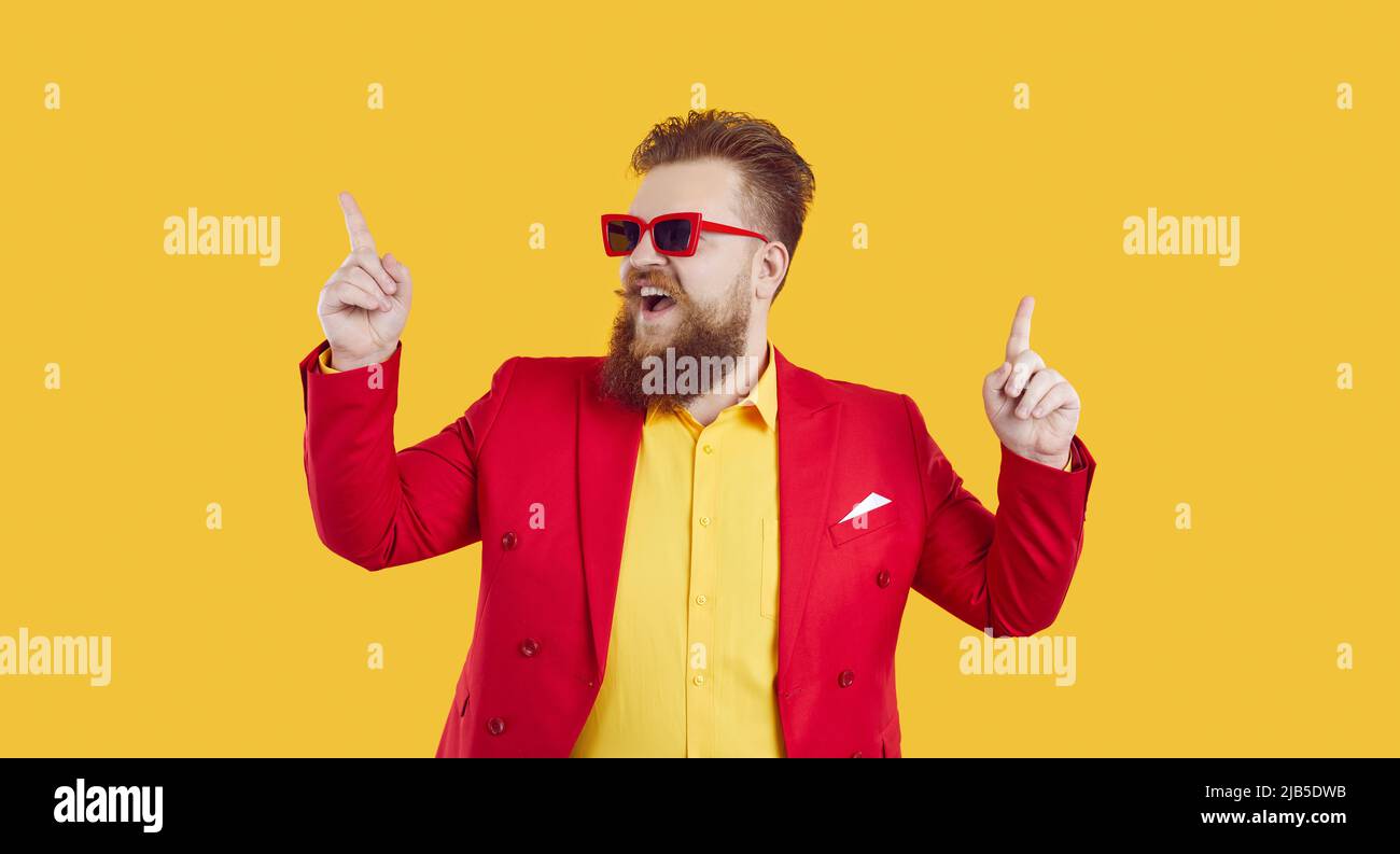 Cheerful and stylish young extravagant chubby man having fun and dancing on yellow background. Stock Photo