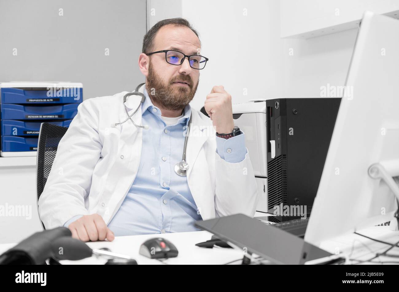 Portrait of friendly smiling healthcare professional therapist sitting at workplace. Happy confident male doctor physician wearing white medical coat Stock Photo