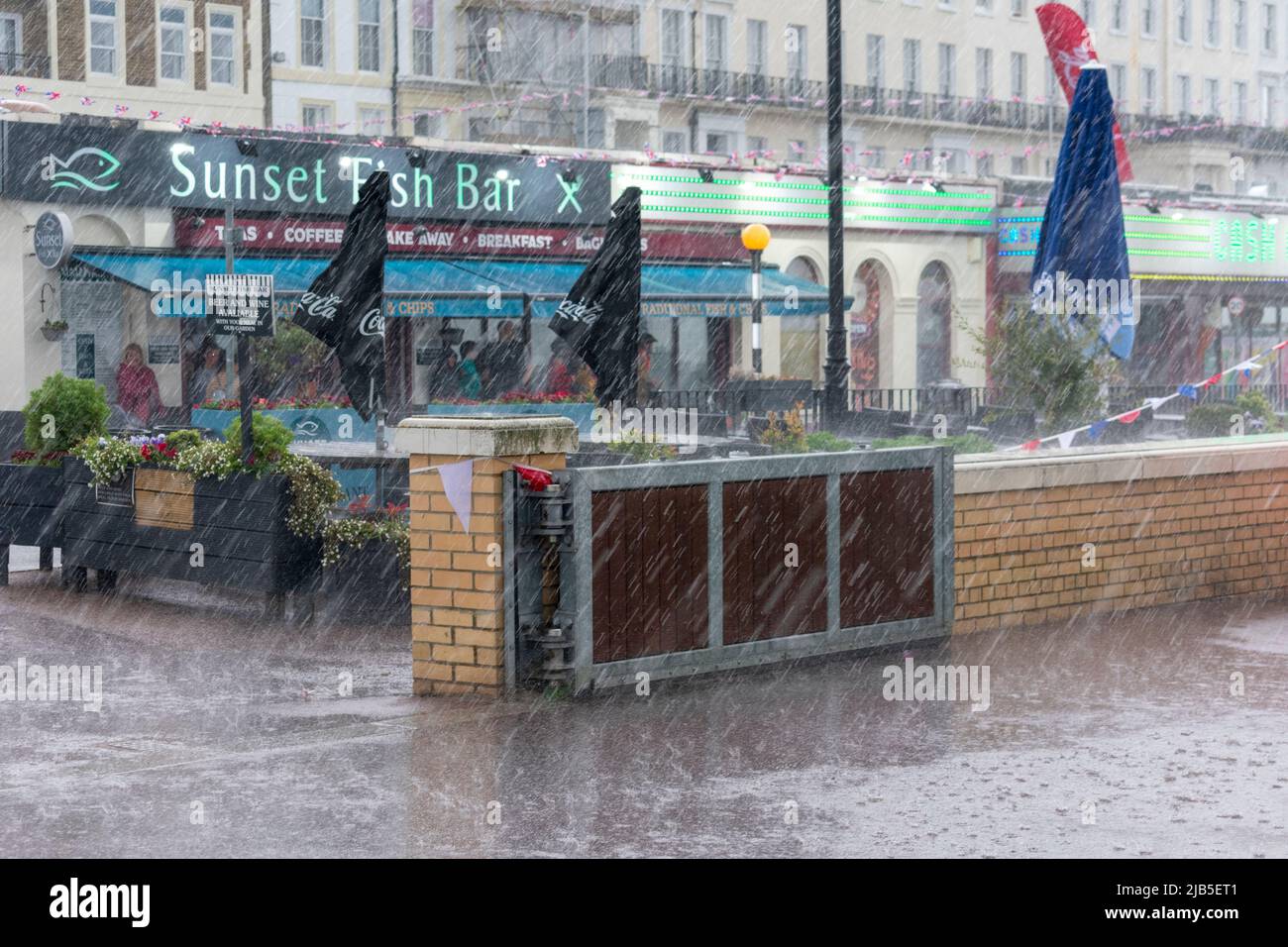 A downpour spoils the afternoon at Herne Bay with rain lashing down onto the promenade, forcing people to shelter. Stock Photo