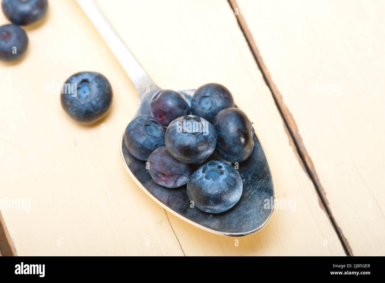 fresh blueberry on silver spoon over a white rustic wood table. Stock Photo