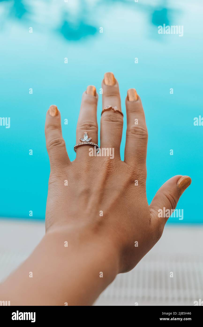 Female hand with ring jewelry on swimming pool blured background