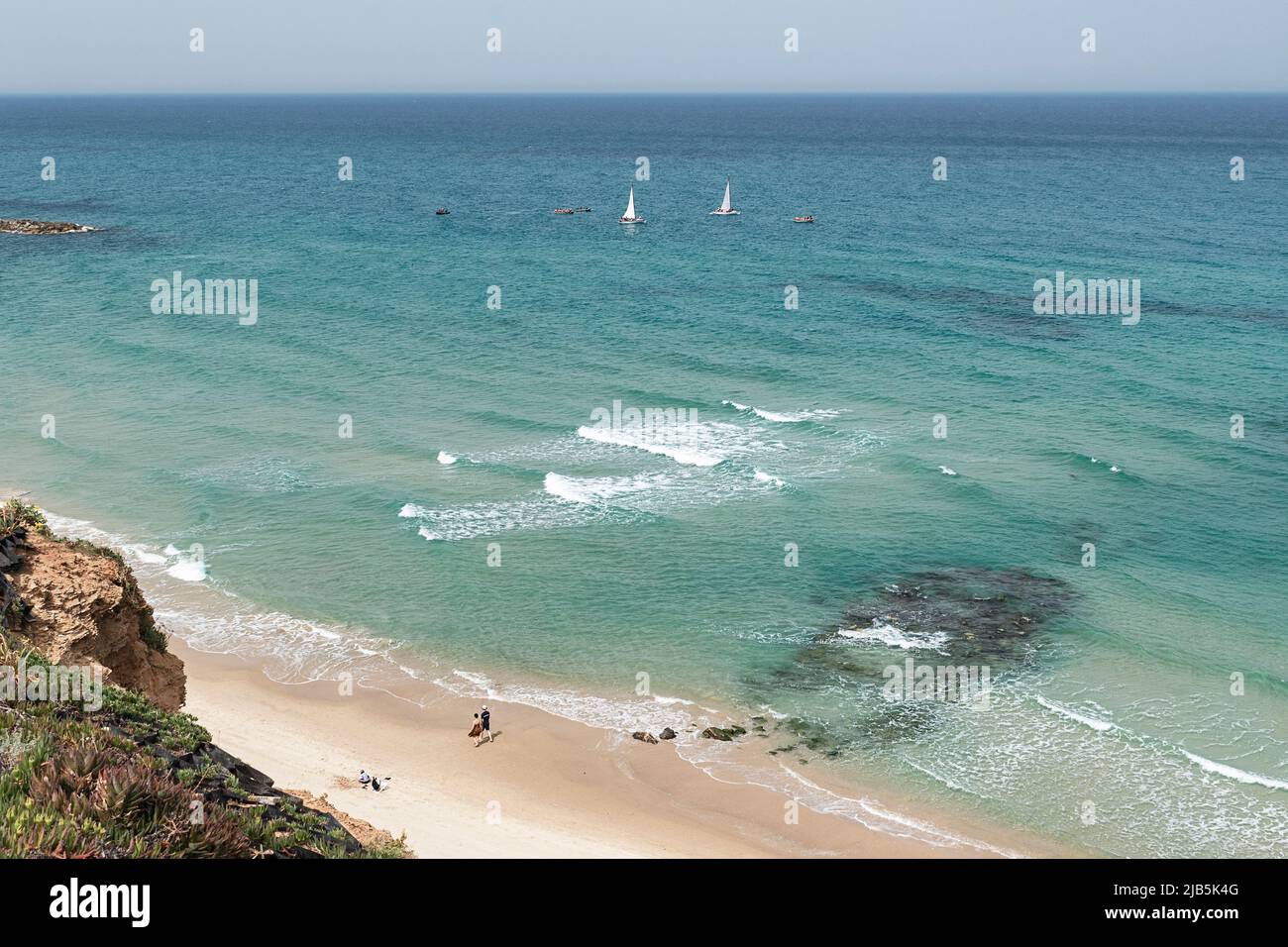 looking down from the cliff onto the eastern Mediterranean Beach at Netanya in Israel with people on the beach and small boats sailing in the sea Stock Photo