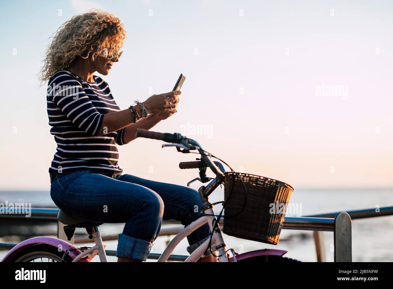 Side view of adult woman using mobile phone connection to messaging sitting on a classic bike. Green transport environment lifestyle. Female people Stock Photo