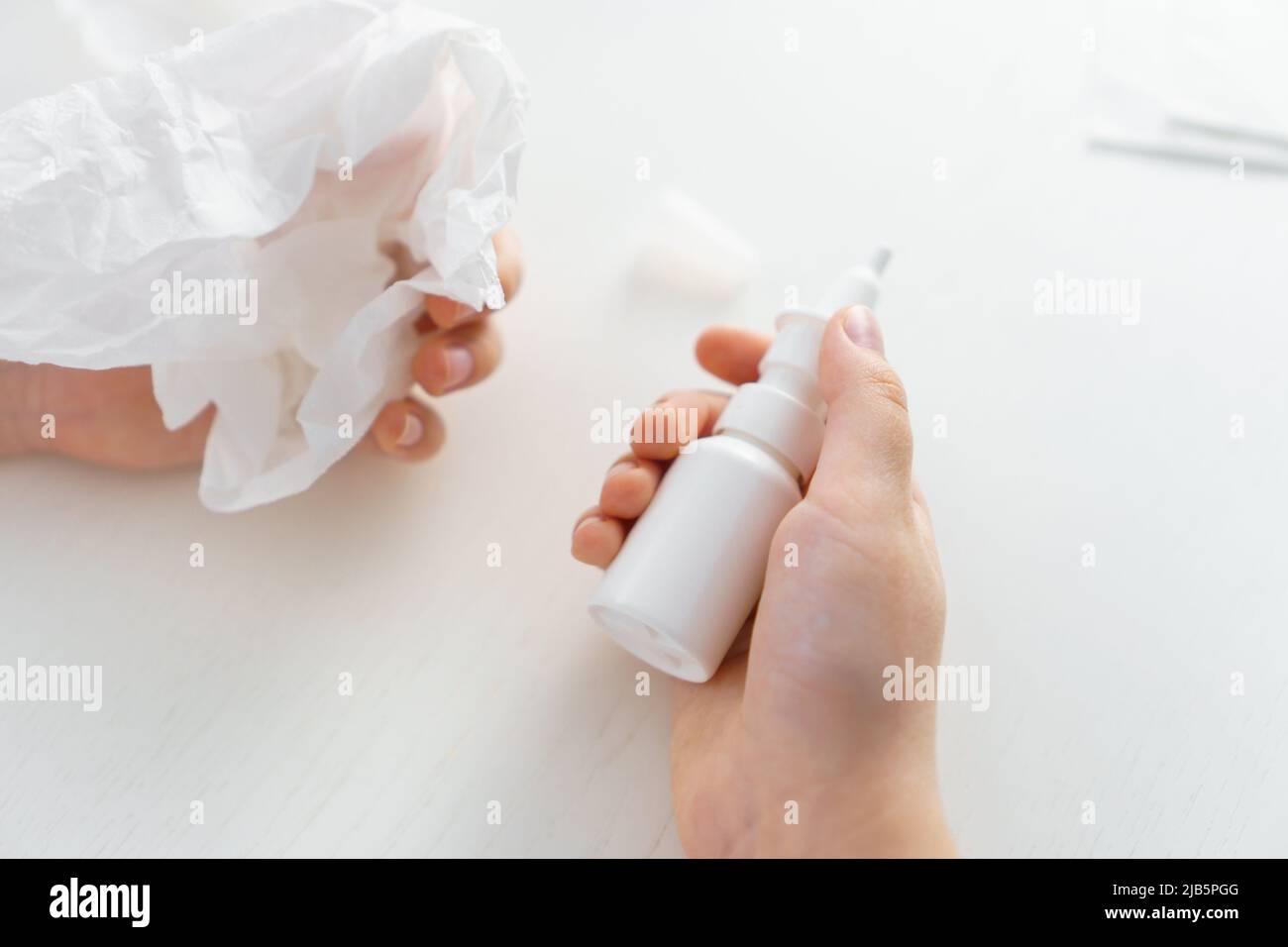 Child hands hold bottle nose spray and paper tissue on white background. Runny nose treatment Stock Photo