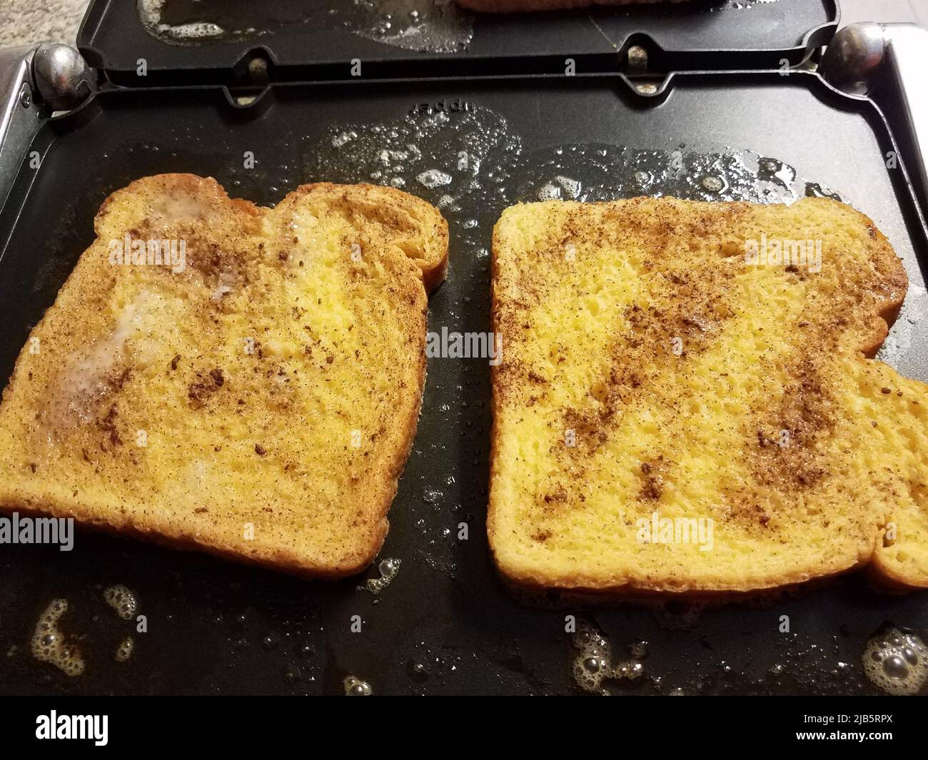 French toast bread with egg and cinnamon cooking on grill or griddle. Stock Photo