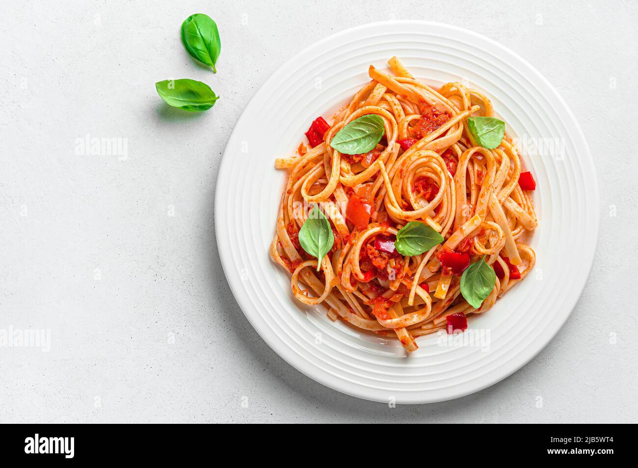 Linguini pasta with tomato sauce and basil on a gray background with a
