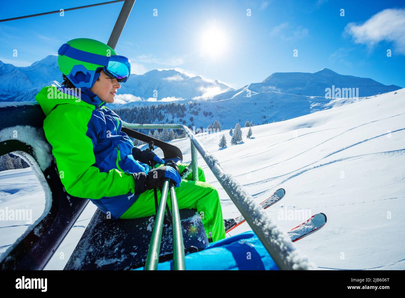 Boy sit in helmet, mask with ski on chairlift over mountains Stock Photo