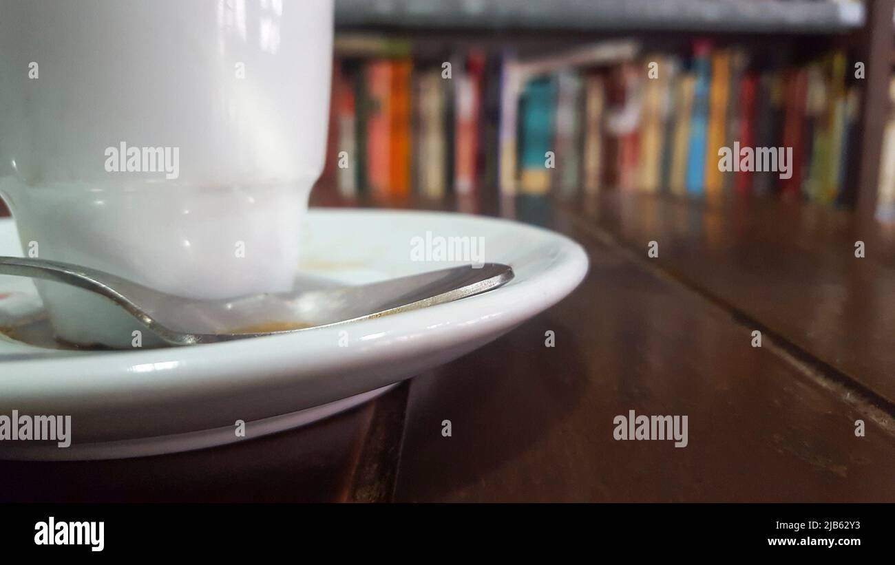 Little coffee cup over wooden table with book shelves background. Selective focus. Stock Photo