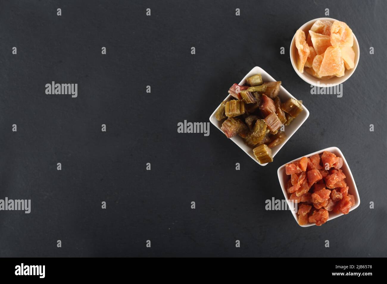 Healthy eating concept - white bowls of candied rheum, pumpkins and cantaloup (rock melon) isolated on black background flat lay. Image contains copy Stock Photo