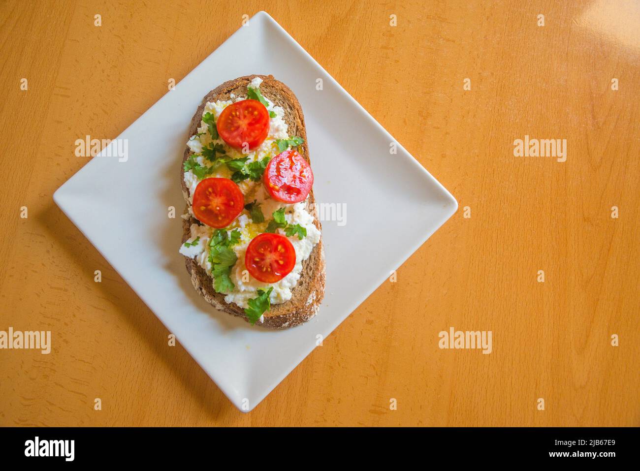 Cottage cheese with cherry tomatoes, olive oil and parsley on toast. Stock Photo