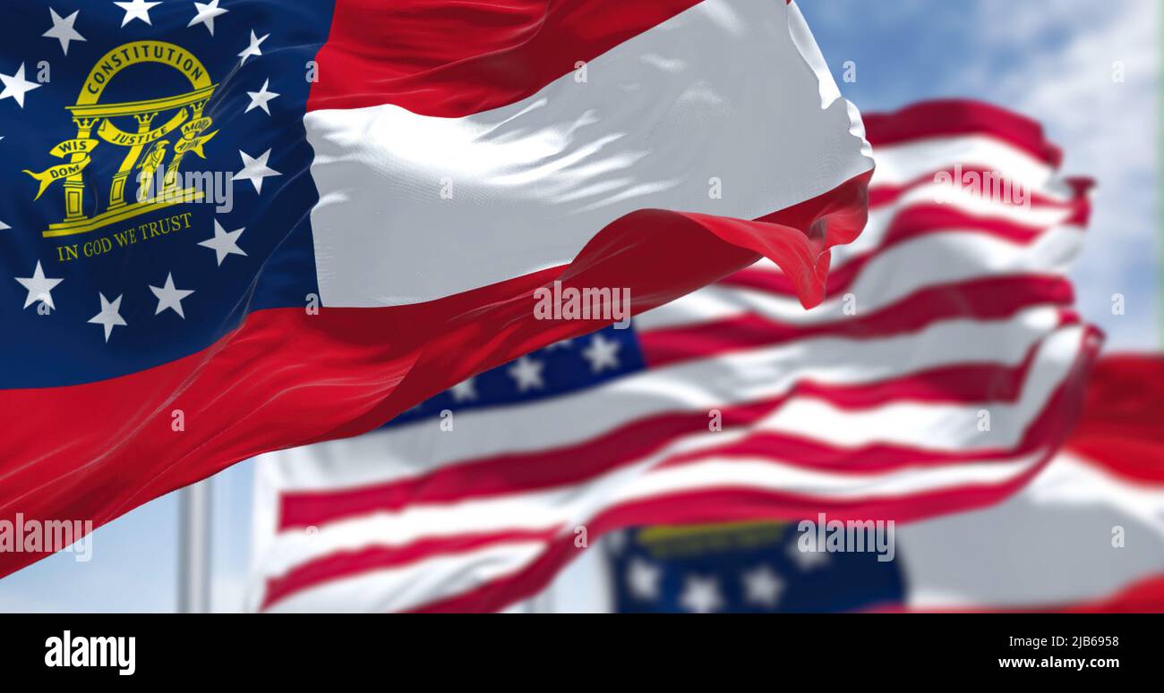 The Georgia state flag waving along with the national flag of the United States of America. In the background there is a clear sky. Stock Photo