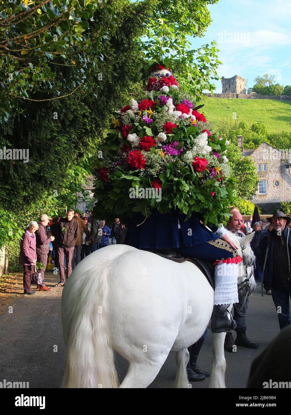 The Castleton Garland King wearing a hooped garland of flowers rides on horseback at ancient Castleton Garland Ceremony 2022 with Peveril Castle in bg Stock Photo