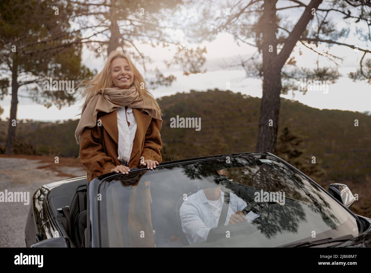 Beautiful Caucasian young woman standing on seat in convertible car with husband and smiling Stock Photo