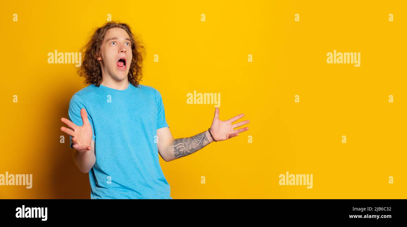 Shocked, surprised young emotional man with long curly hair shouting ...