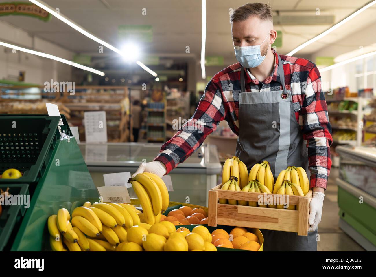 Seller in apron and mask holding bananas at market, male salesman staking fruit bananas in supermarket Stock Photo