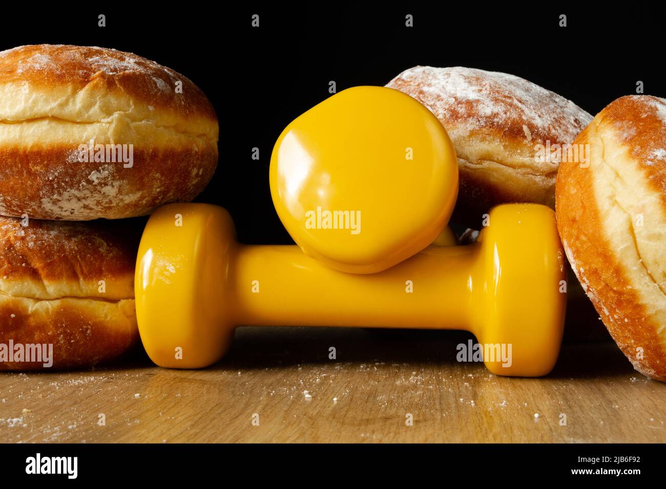 Dumbbells and Polish pączki deep-fried doughnuts. Fat thursday pączek, traditional feast day in Poland. Healthy fitness gym workout. Stock Photo