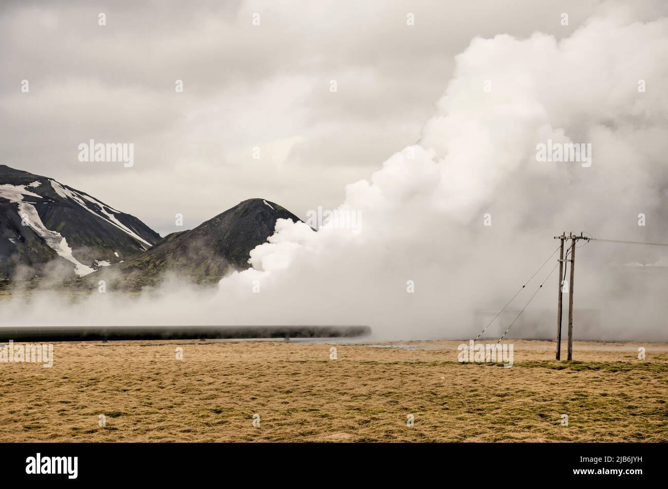 Hengill, Iceland, April 22, 2022: hot steam coming out of the ground in a grassy landscape with power lines near the Hellisheiði geothermal power plan Stock Photo
