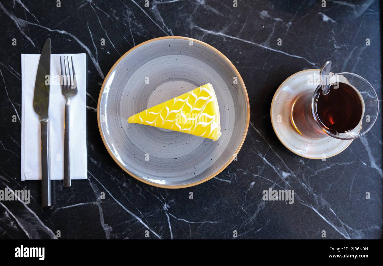 Slice of lemon cheesecake on a plate with traditional Turkish tea, top table view over black white pattern background. Stock Photo
