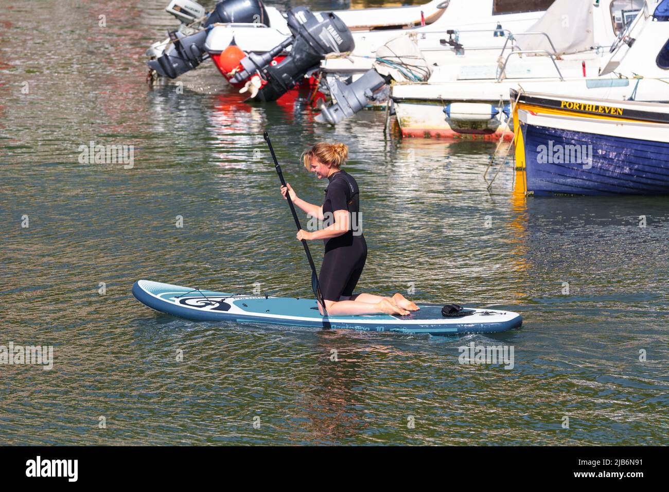 Woman in a wetsuit kneeling on her paddle board as he she paddles