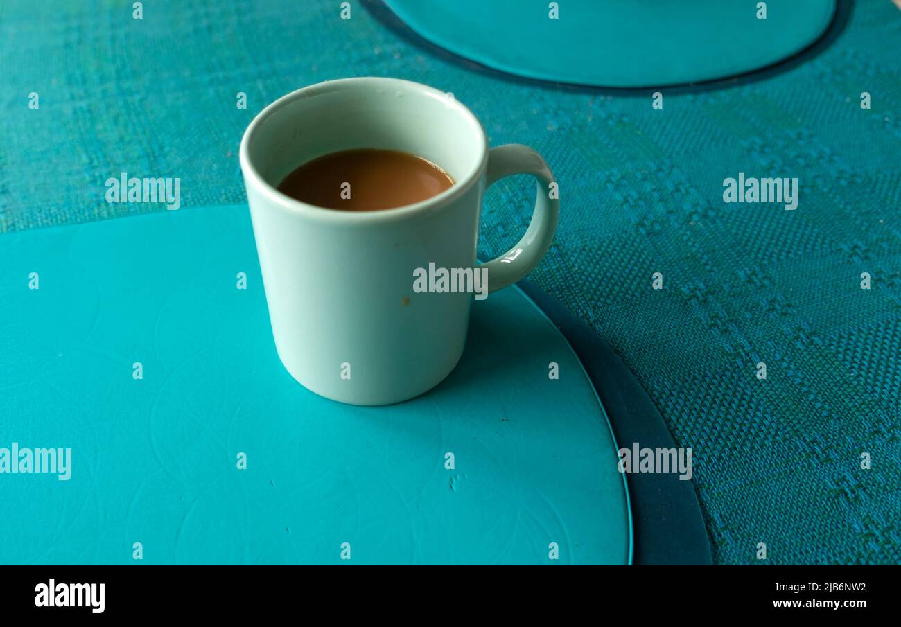 Half drunk single cup of coffee in green cup sitting on table with plastic turquoise place mat and table cloth inside a home UK   KATHY DEWITT Stock Photo